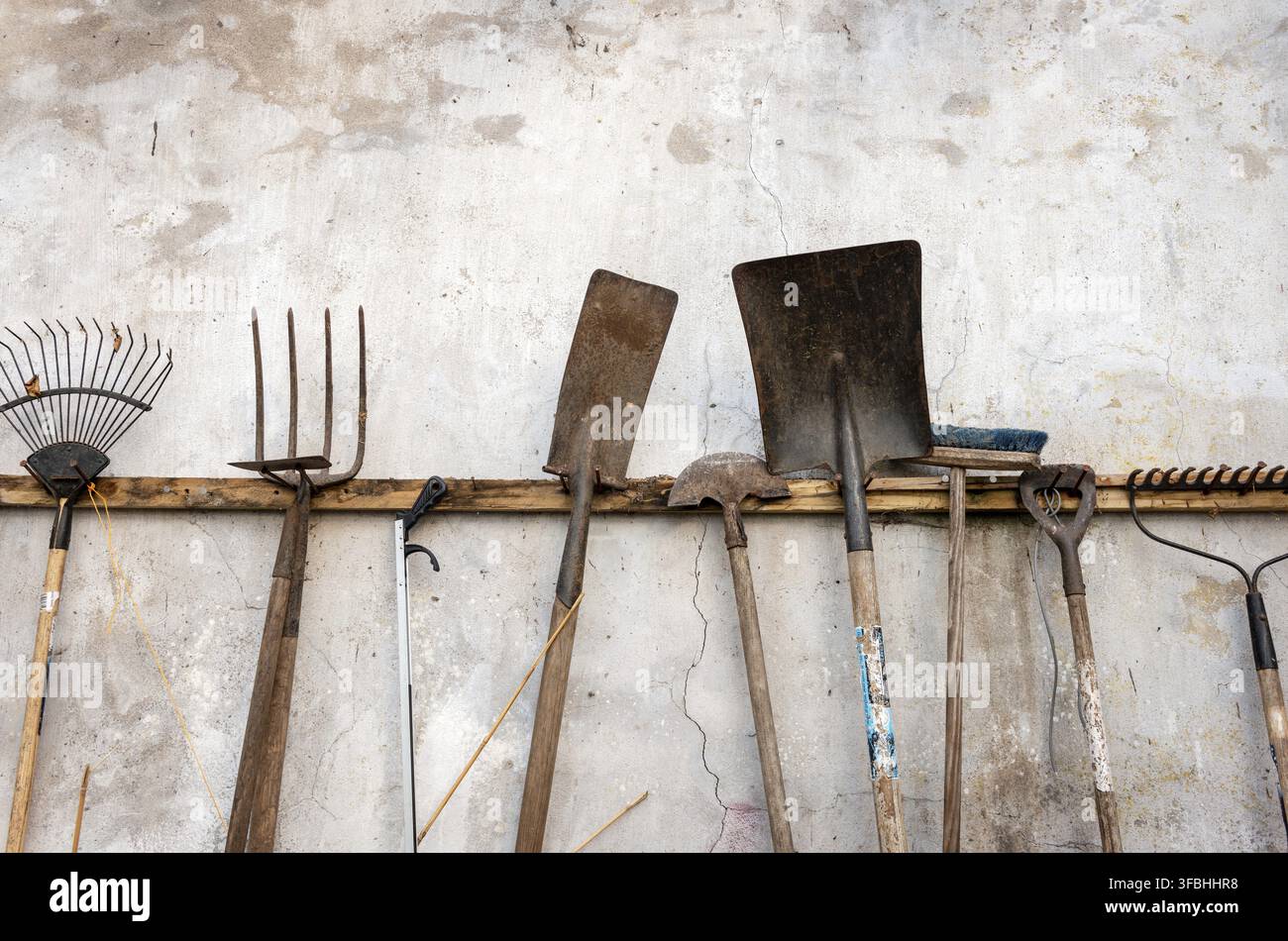 A collection of various used rusty garden tools hanging on white wall Stock Photo