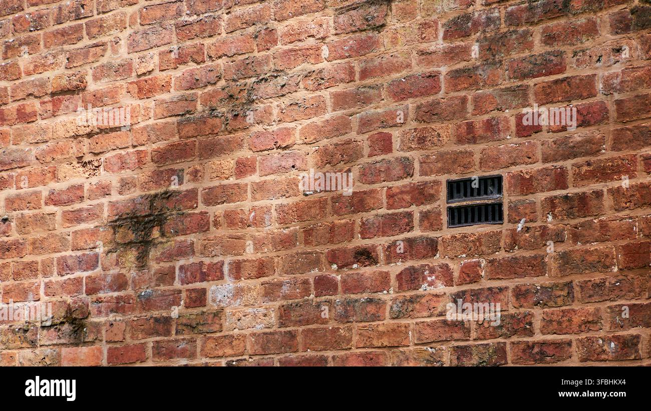 a redbrick wall with vent and shadows, full frame. Stock Photo