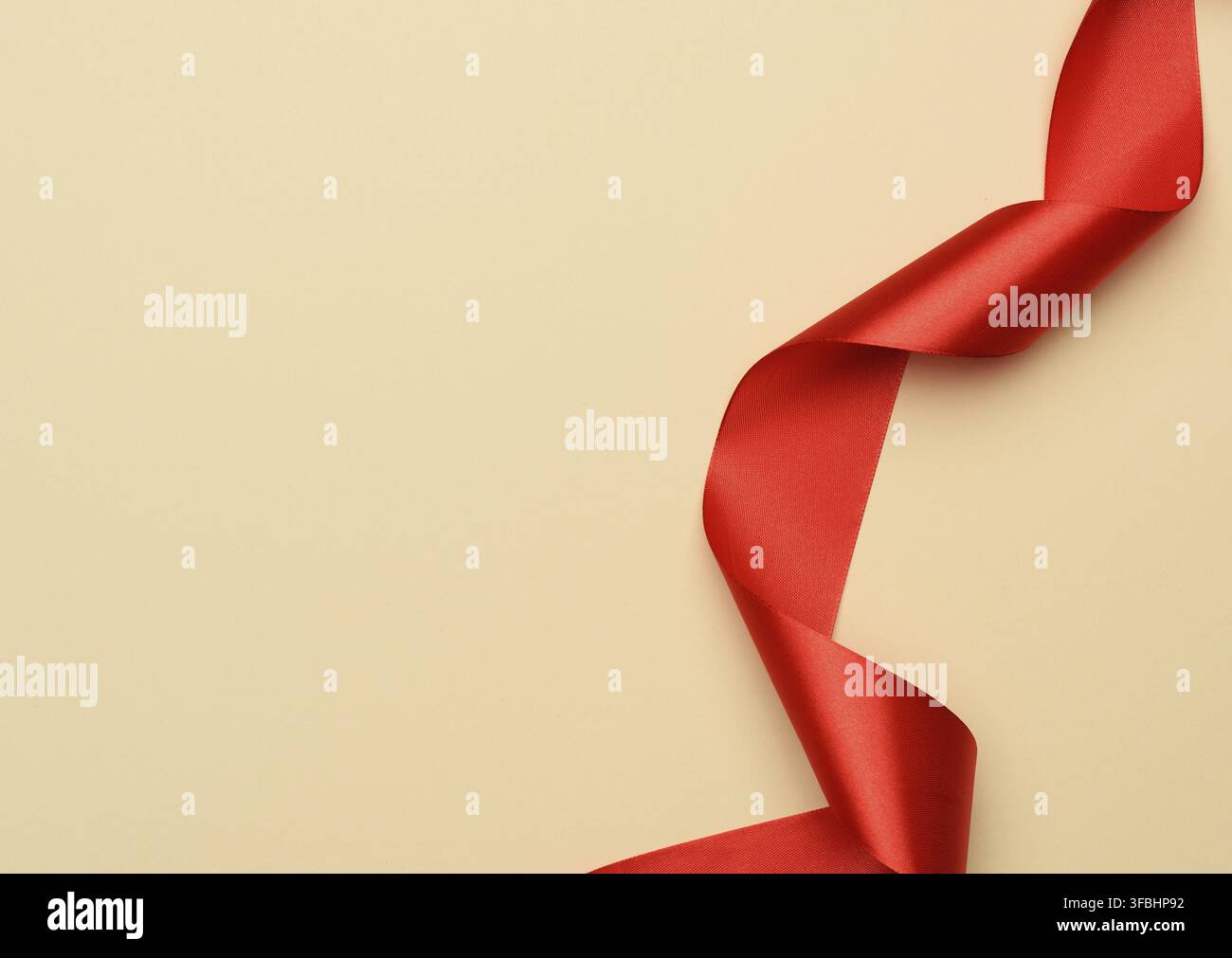 Curled red silk ribbon on a beige background, copy space Stock Photo