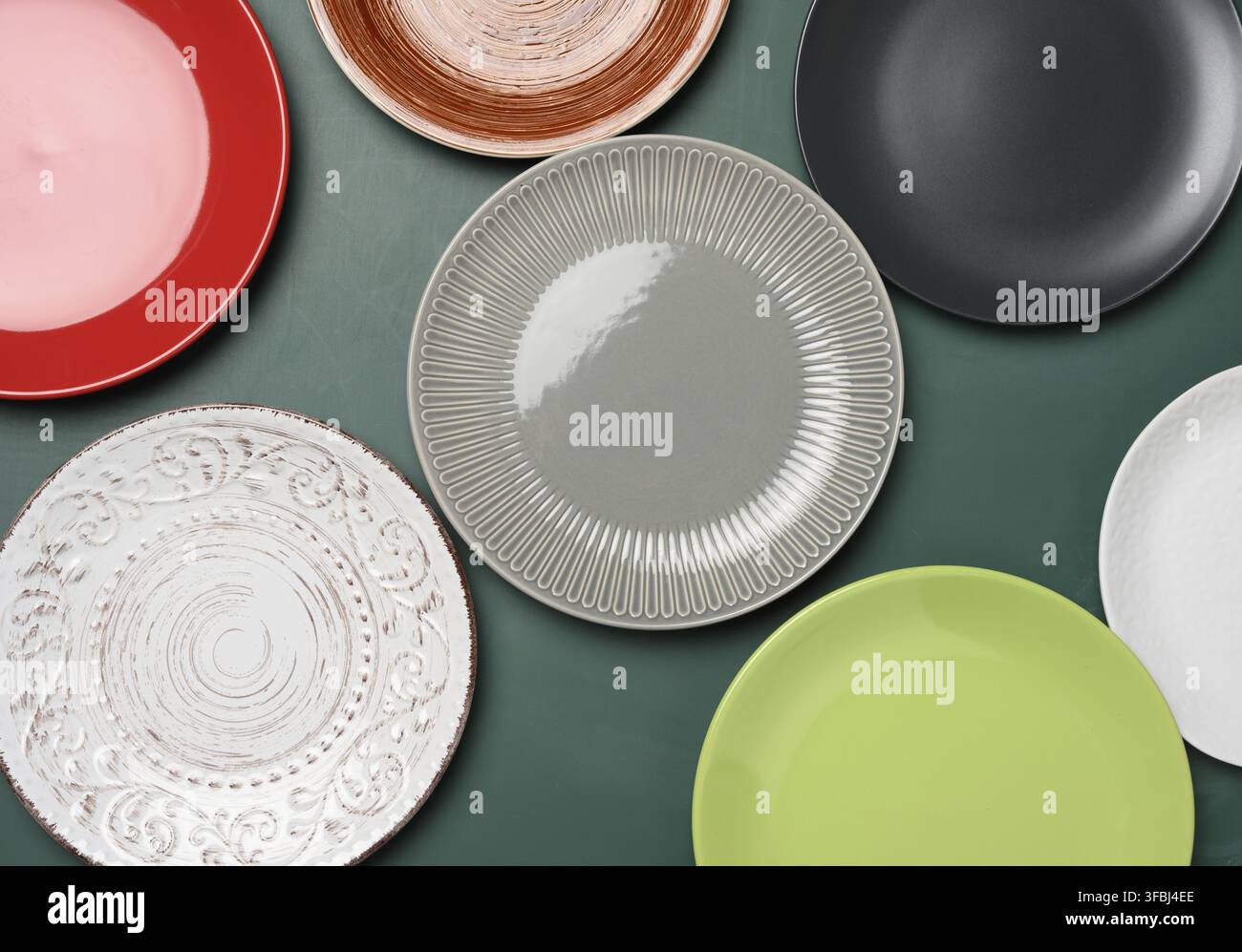 Empty round multicolored ceramic plates on green background, top view Stock Photo