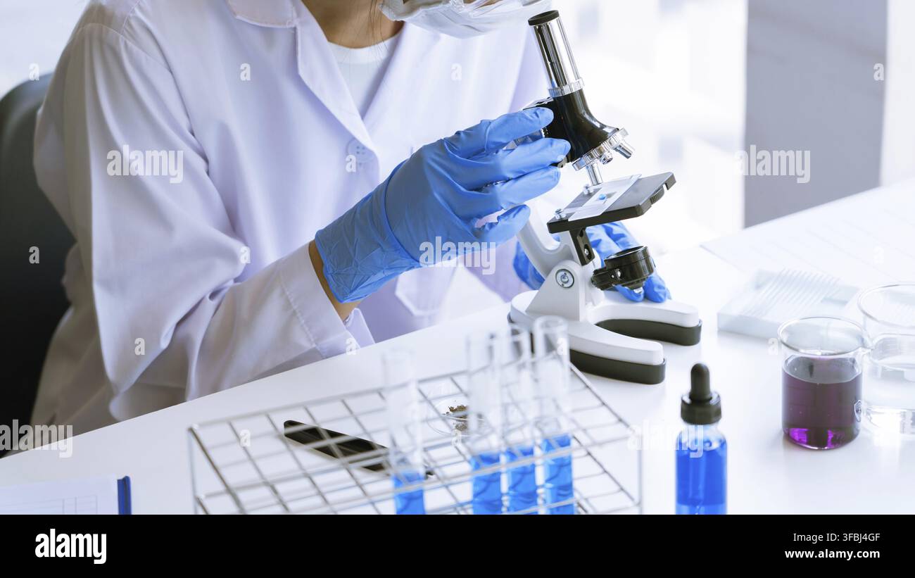 Young Asian scientist Working looking through a microscope doing research for analyzing a Experiments sample in a forensic laboratory Stock Photo