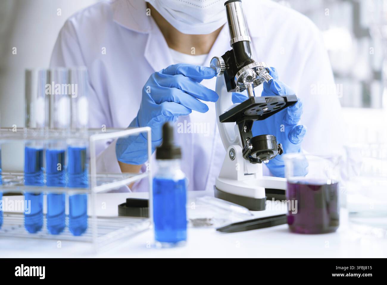Young Asian scientist Working looking through a microscope doing research for analyzing a Experiments sample in a forensic laboratory Stock Photo