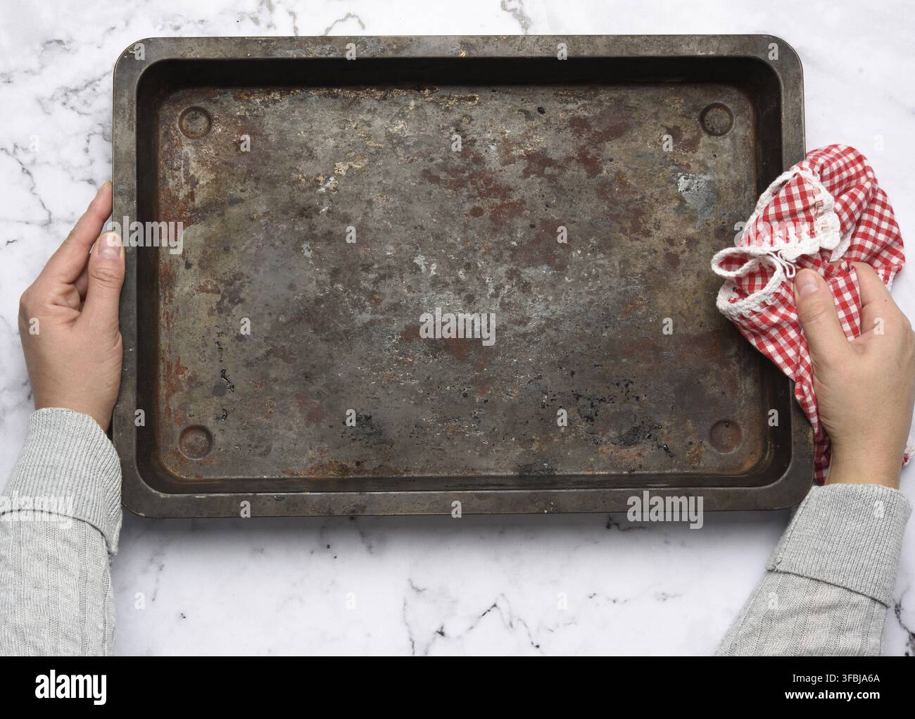Hand hold empty metal rectangular baking sheet on a white table, top view Stock Photo
