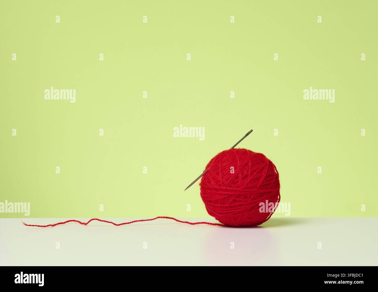Red ball with woolen thread on white table, green background Stock Photo