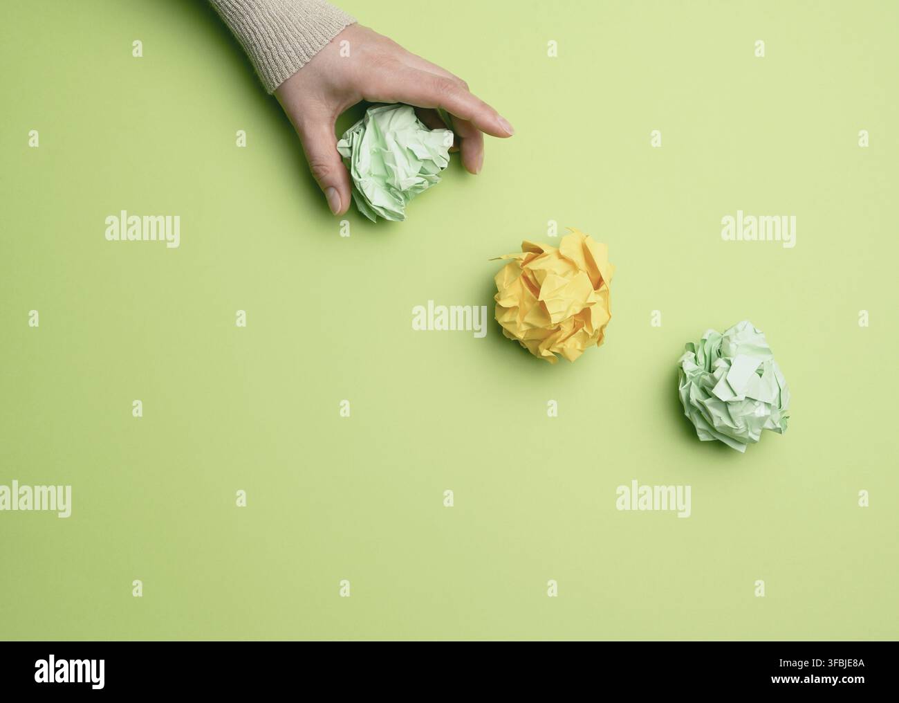 Three crumpled balls of colored paper on a green background, hand throws paper Stock Photo