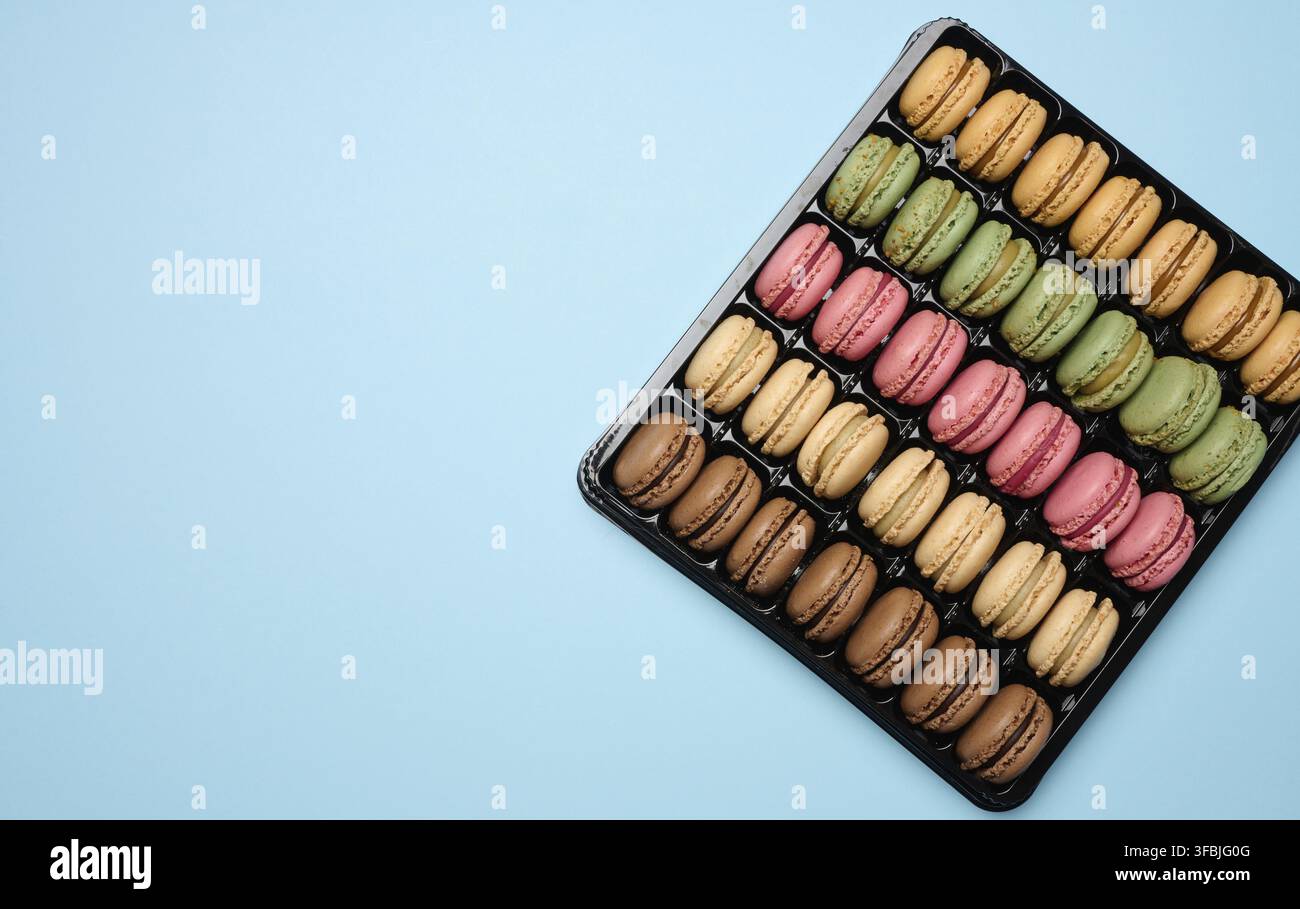 Multi-colored macarons on a blue background in a plastic box, top view. Copy space Stock Photo
