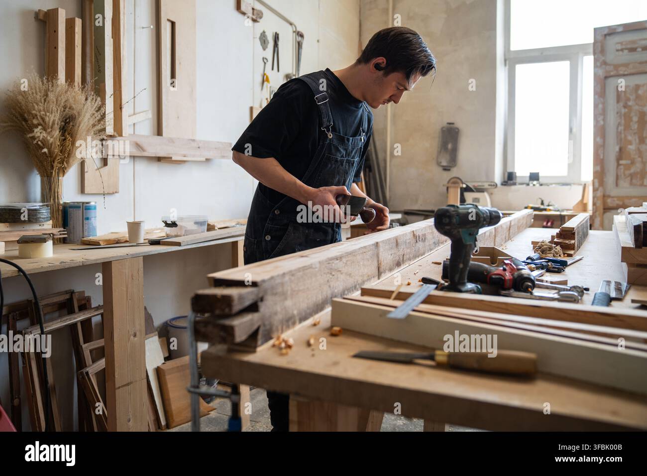 Professional craftsperson restoring window frame in workshop, using hand plane tool at workbench. Stock Photo