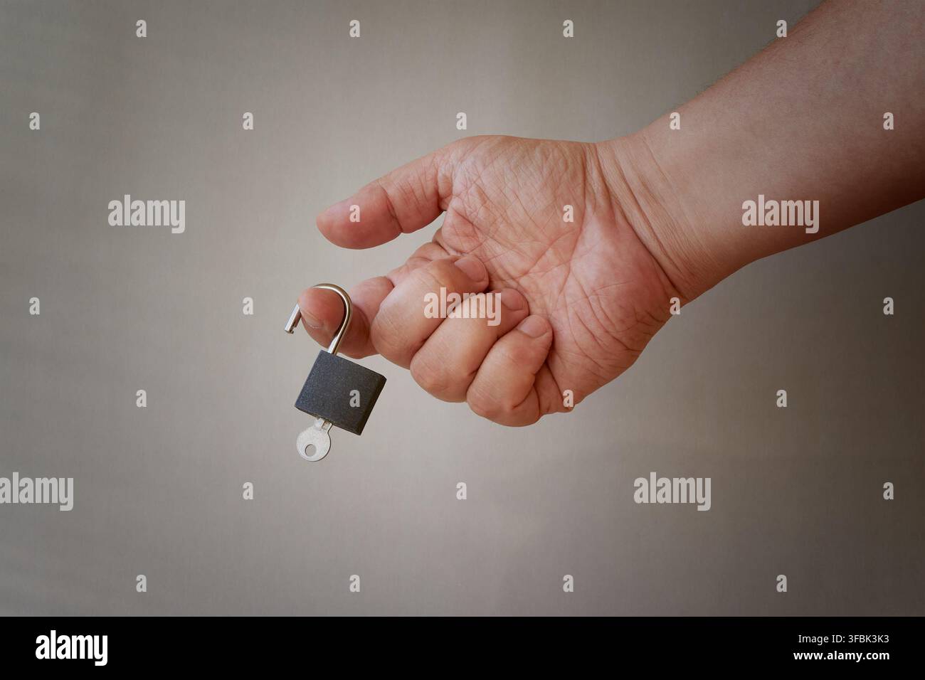 A person's hand holds a small padlock with a key. Stock Photo