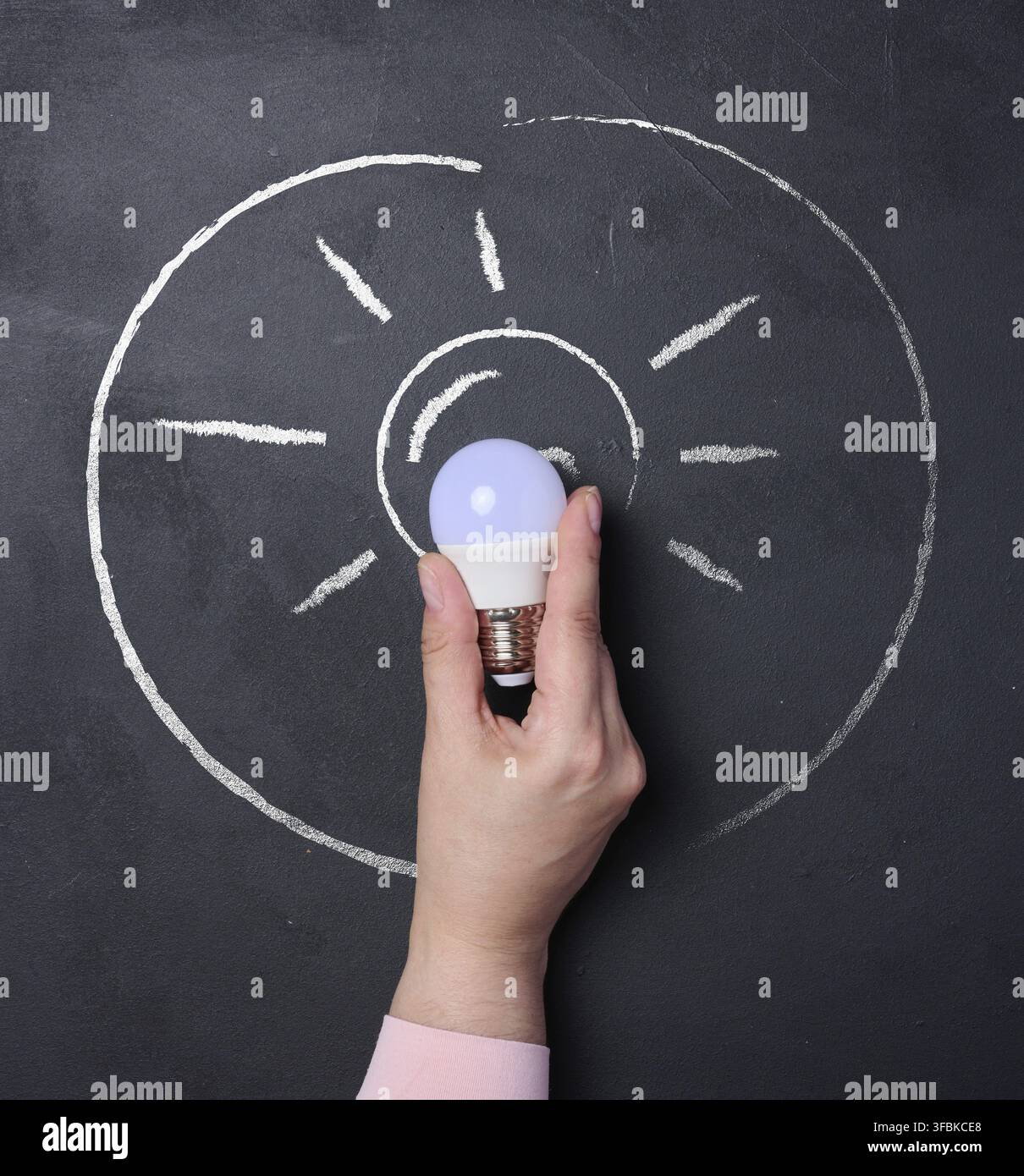 A human hand holding a light bulb, a chalk outline of the bulb with rays. Concept of a new idea Stock Photo
