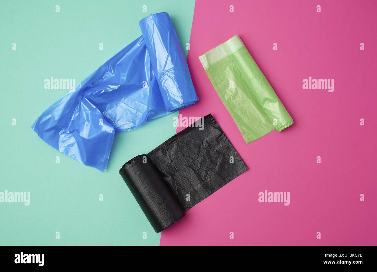 Three rolled up rolls with plastic garbage bags on a green pink background, top view Stock Photo