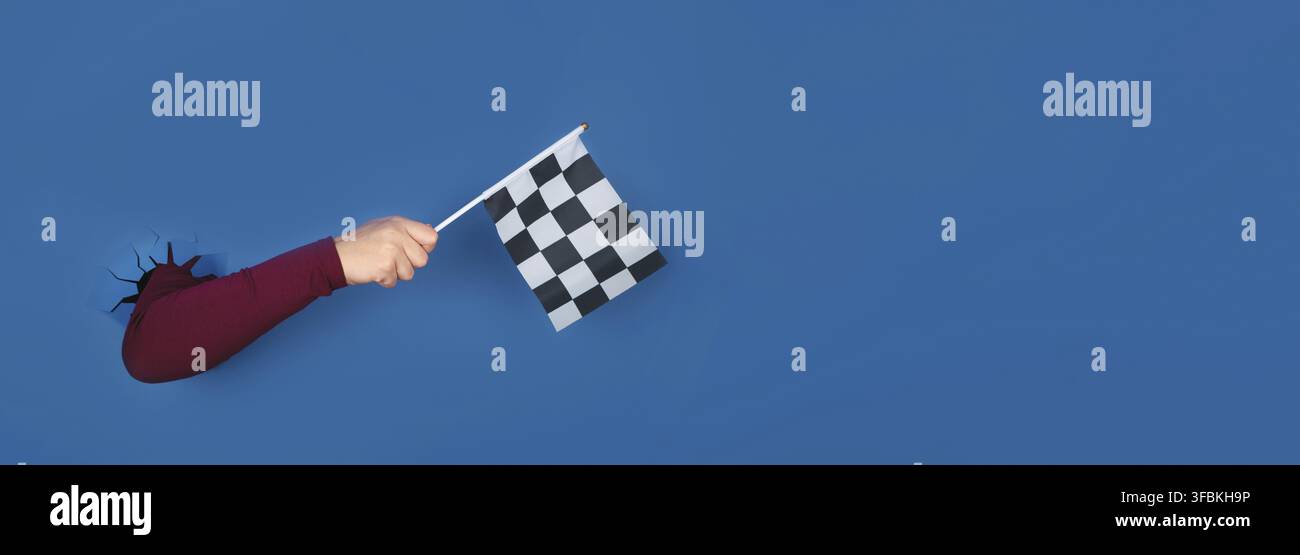Hand holding checkered flag over blue background, panoramic layout Stock Photo
