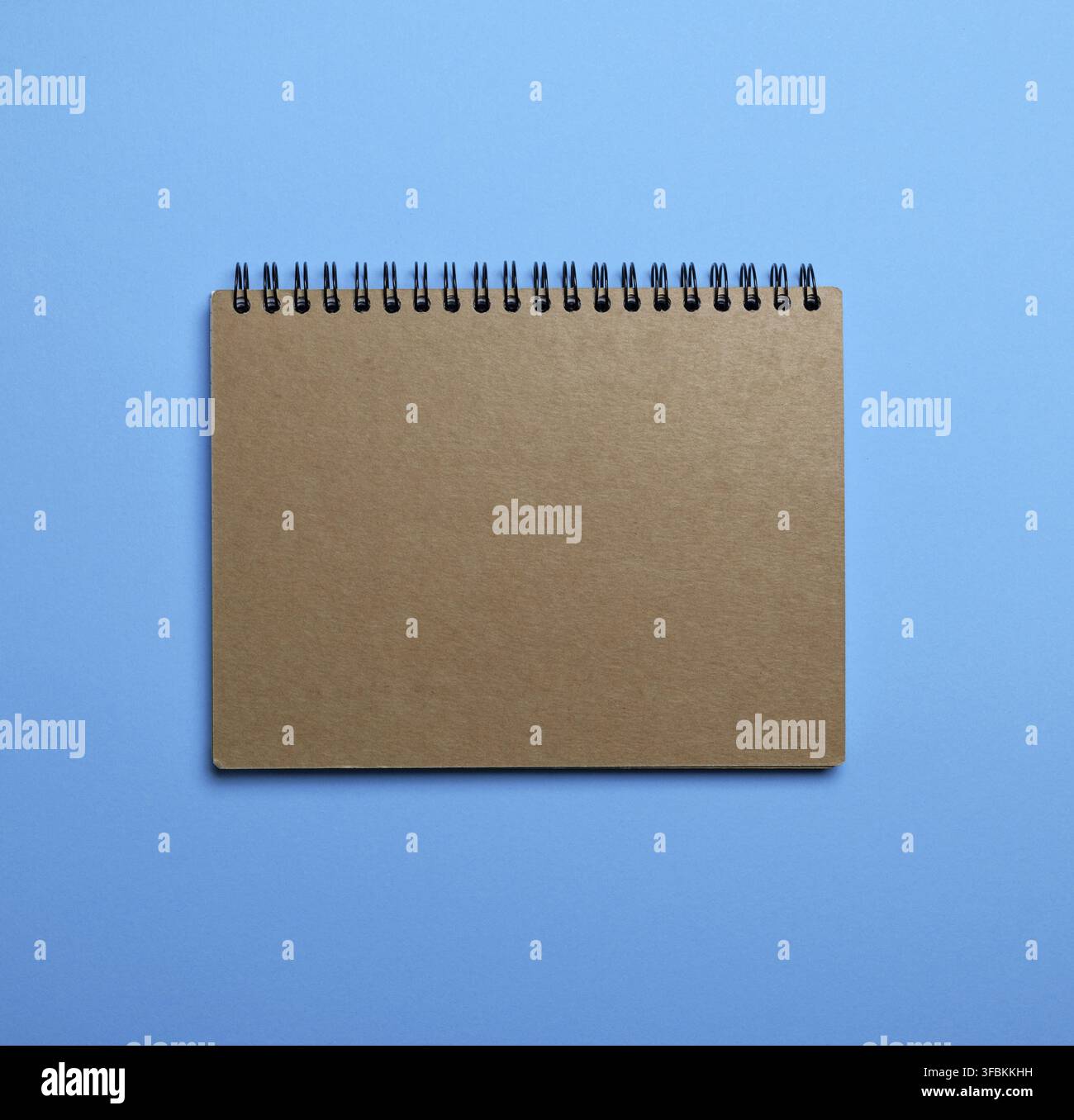 Notebook on a black iron spring with brown empty sheets on a blue background, close up Stock Photo