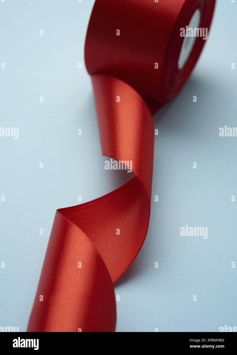 Curled red silk ribbon on blue background, close up Stock Photo