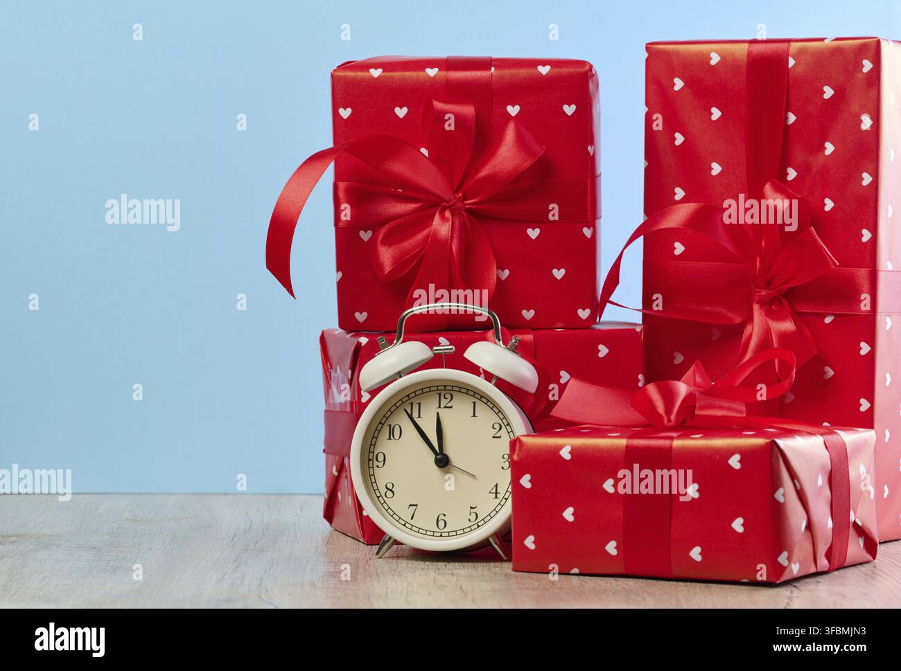 Alarm clock and stack of red gift boxes on blue background Stock Photo