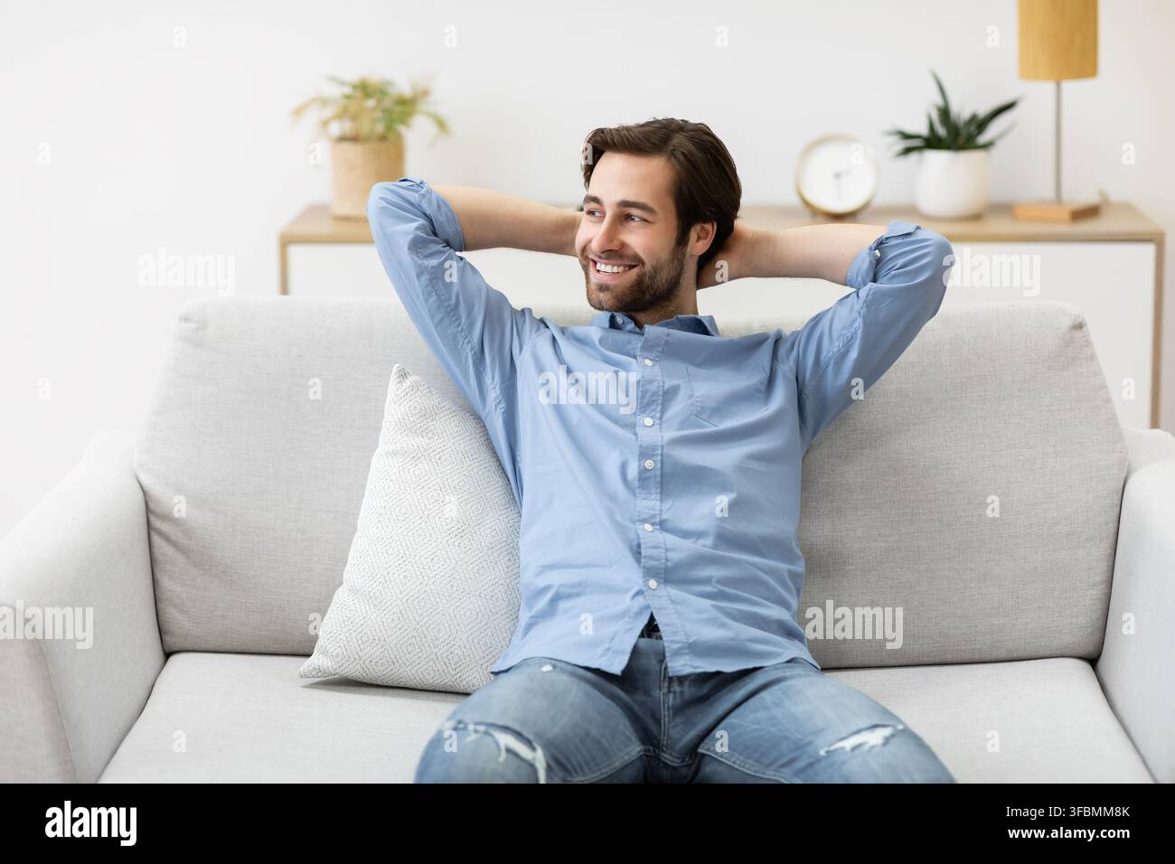 Relaxed Guy Sitting Holding Hands Behind Head On Sofa Indoor Stock Photo
