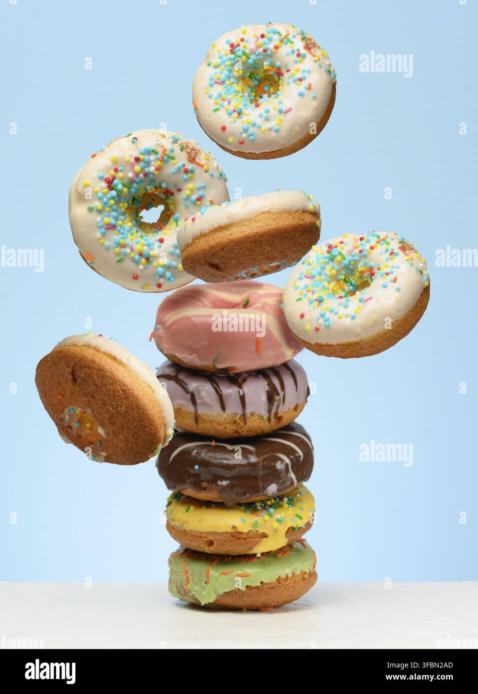 A stack glazed donuts on a table. White donuts with sprinkles flying around them Stock Photo