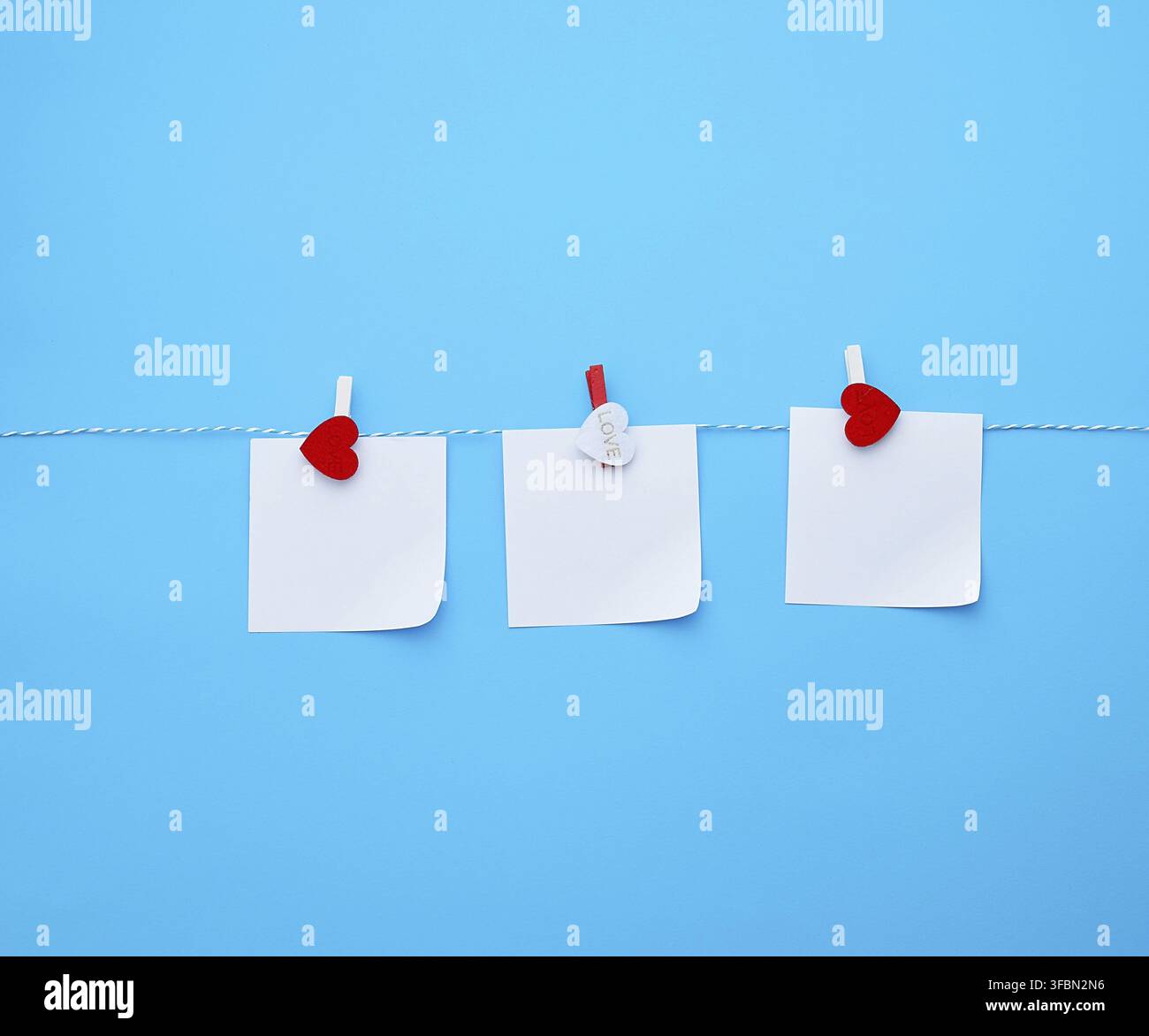 Three empty square white paper sheets hanging on decorative clothespins, blue background Stock Photo