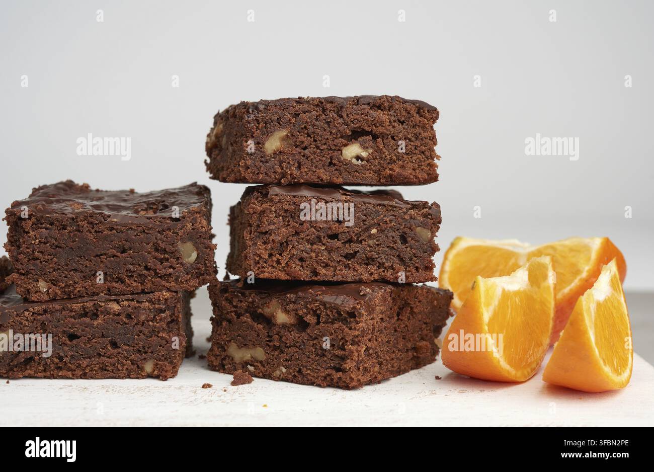 Stack of square baked slices of brownie chocolate cake with walnuts on a white wooden board Stock Photo