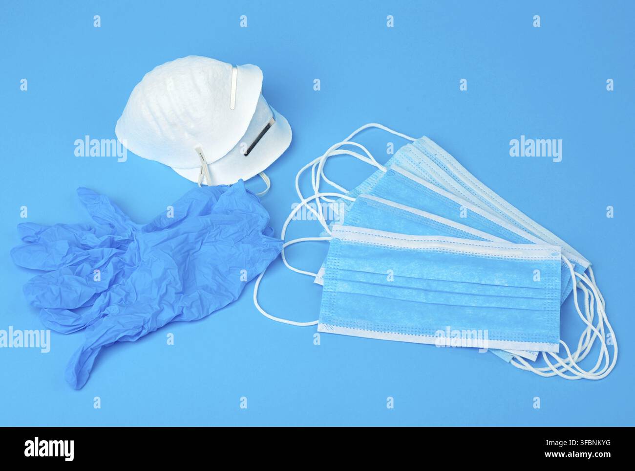 Disposable gloves and stack of medical masks made of non-woven material with white rubber bands on a blue background, protective accessory for the res Stock Photo