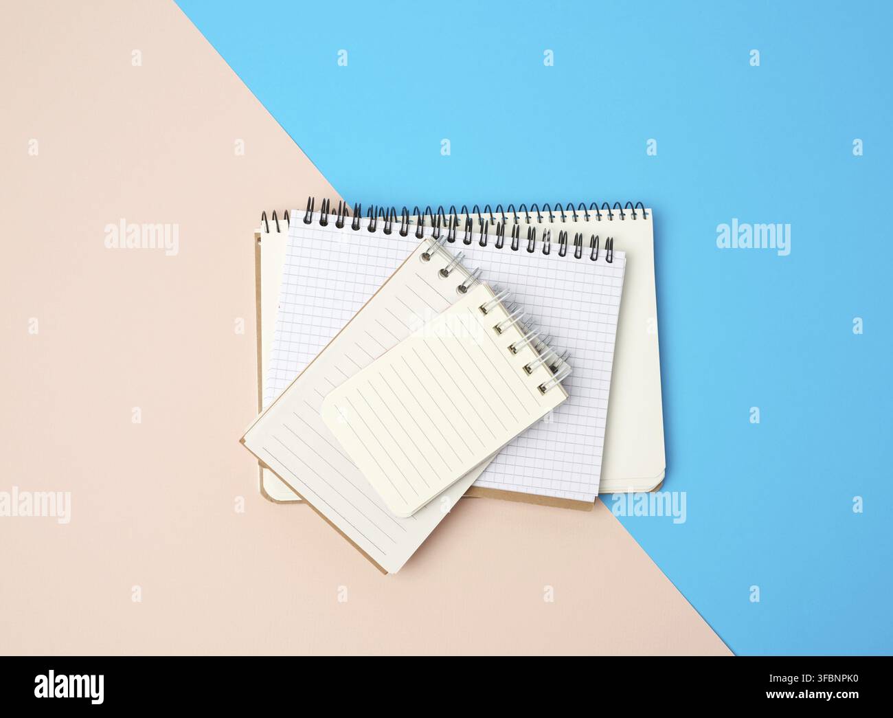 Stack of spiral open notebooks with blank white sheets on a blue background, top view Stock Photo