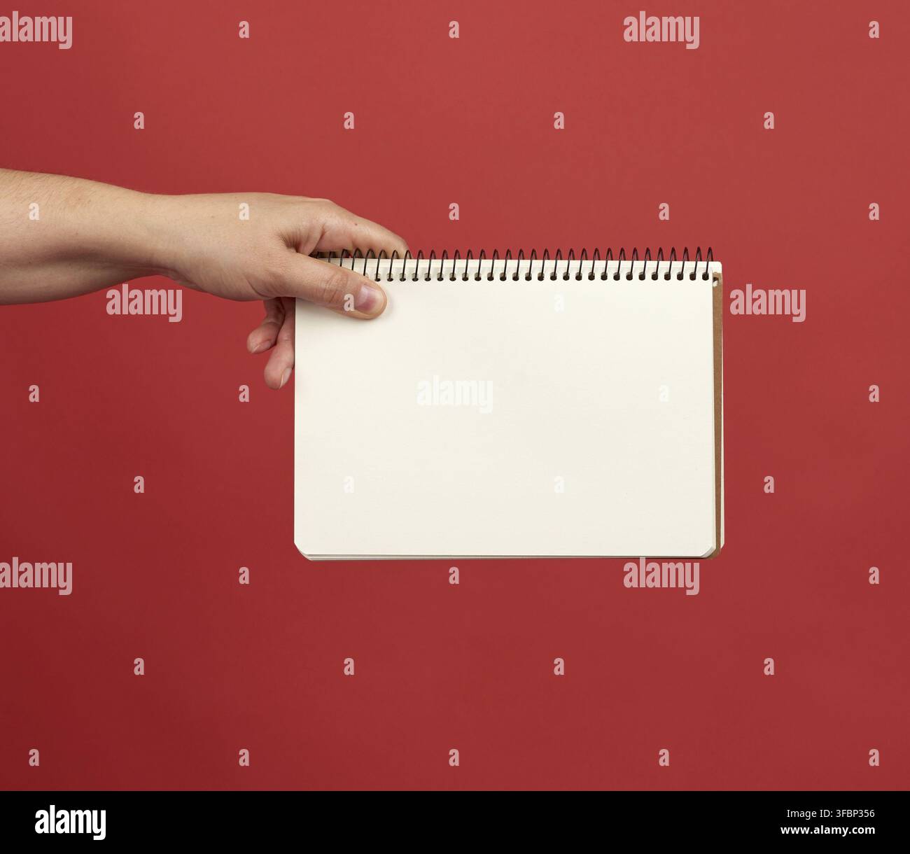Hand holding an open spiral notebook with empty white sheets, red background, copy space Stock Photo