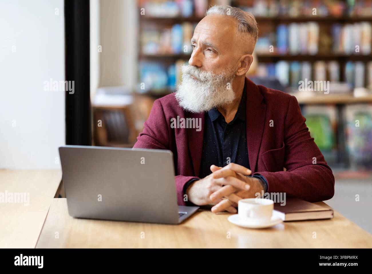 Pensive grey-haired businessman using laptop at cafe, looking through window Stock Photo