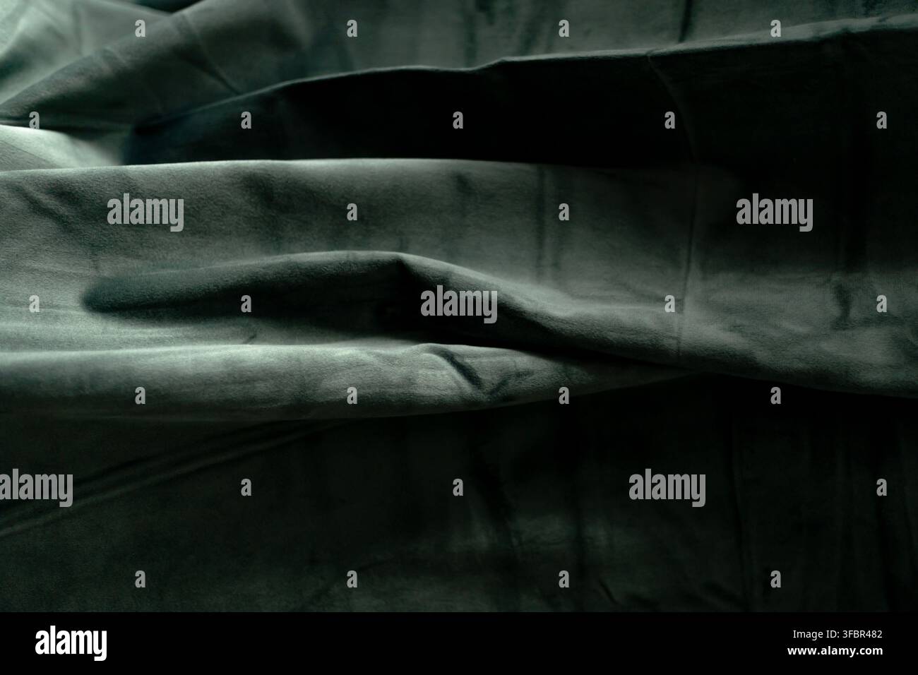 Close up of draped dark grey velvet cloth showing deep folds, soft texture, and shadows. Sharp details on the fabric surface. Stock Photo
