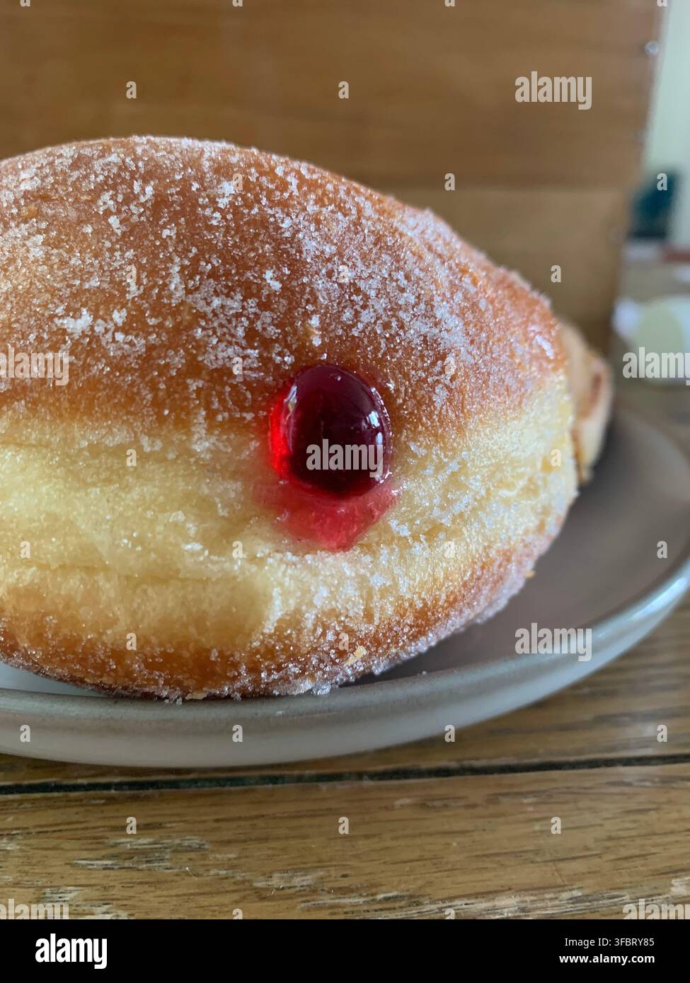 A fresh jam doughnut coated in granulated sugar with strawberry jelly filling oozing out Stock Photo