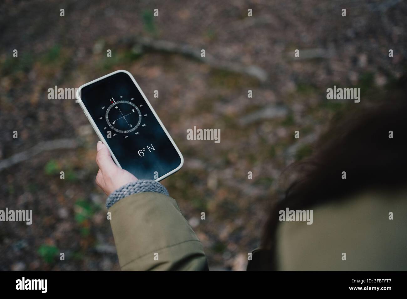 Woman using a digital compass on smartphone for navigation and finding direction while exploring a forest Stock Photo