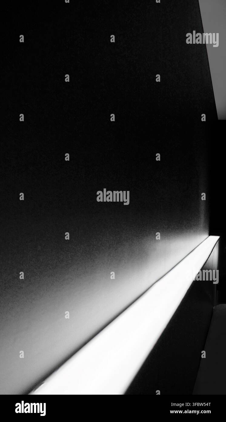 Dramatic architectural background featuring a dark textured wall illuminated by a white LED light strip. The diagonal lighting creates a glowing gradi Stock Photo