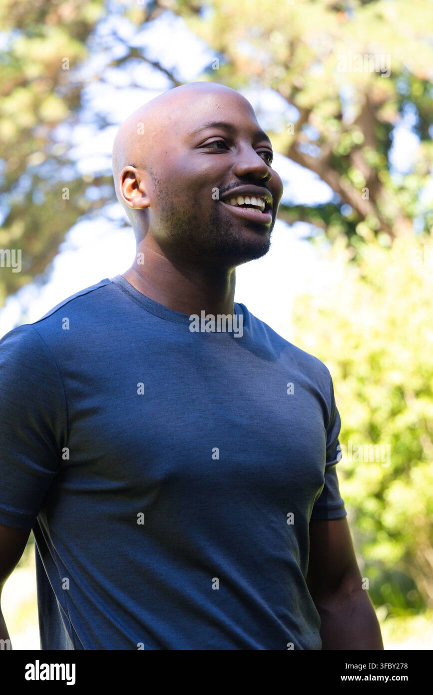 African man smiling and standing while turning slightly to right in park wearing blue T-shirt Stock Photo