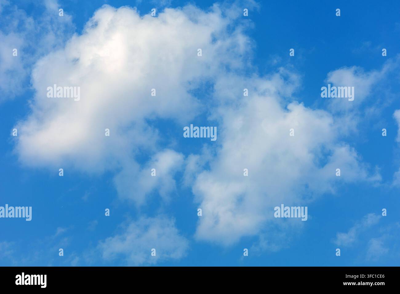 Fluffy white clouds float gently across a bright blue sky on a clear day in Spain. Stock Photo
