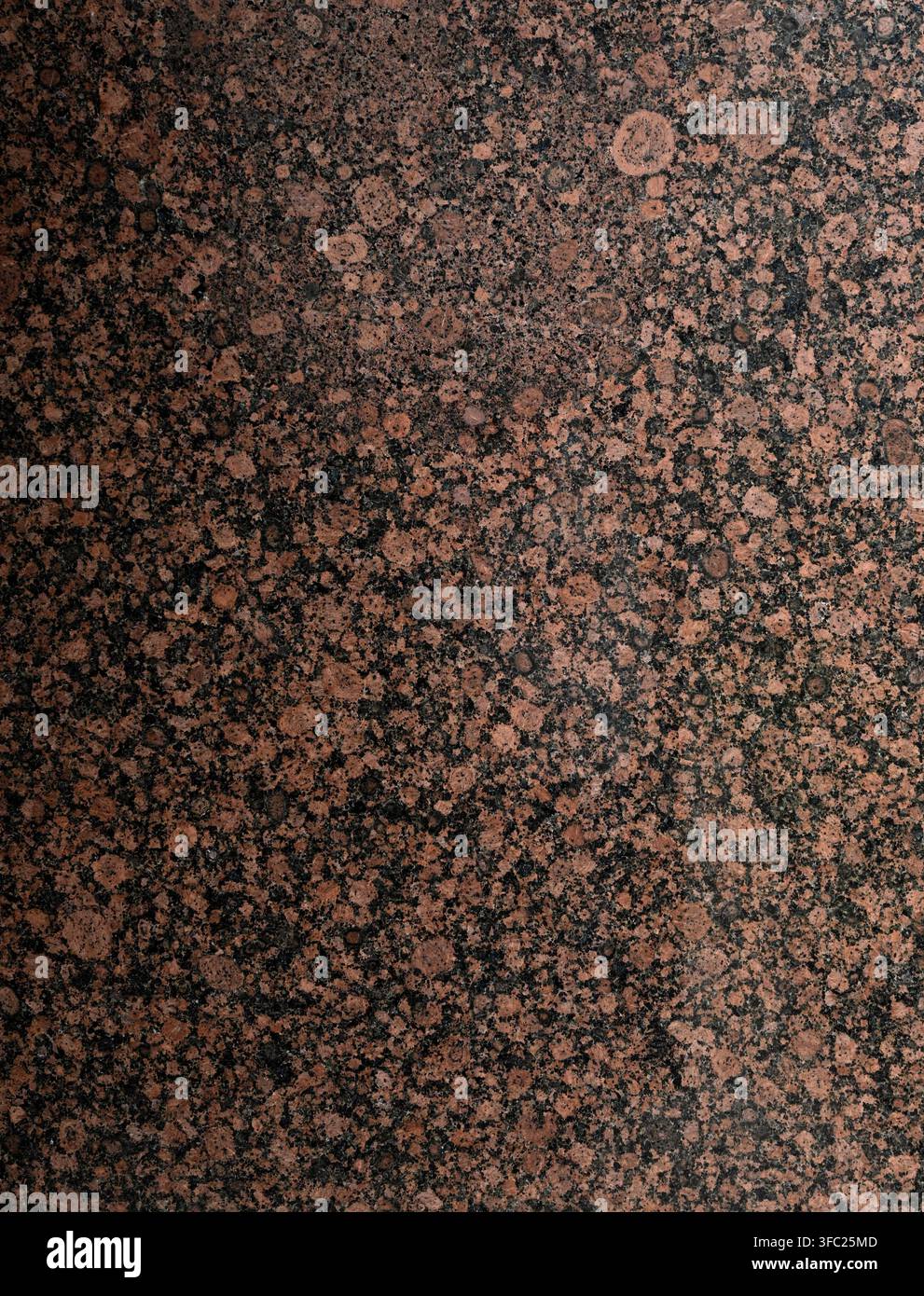Vertical close up of a polished reddish brown granite surface with black splotches, crater‑like circular patches, gray mottled areas Stock Photo