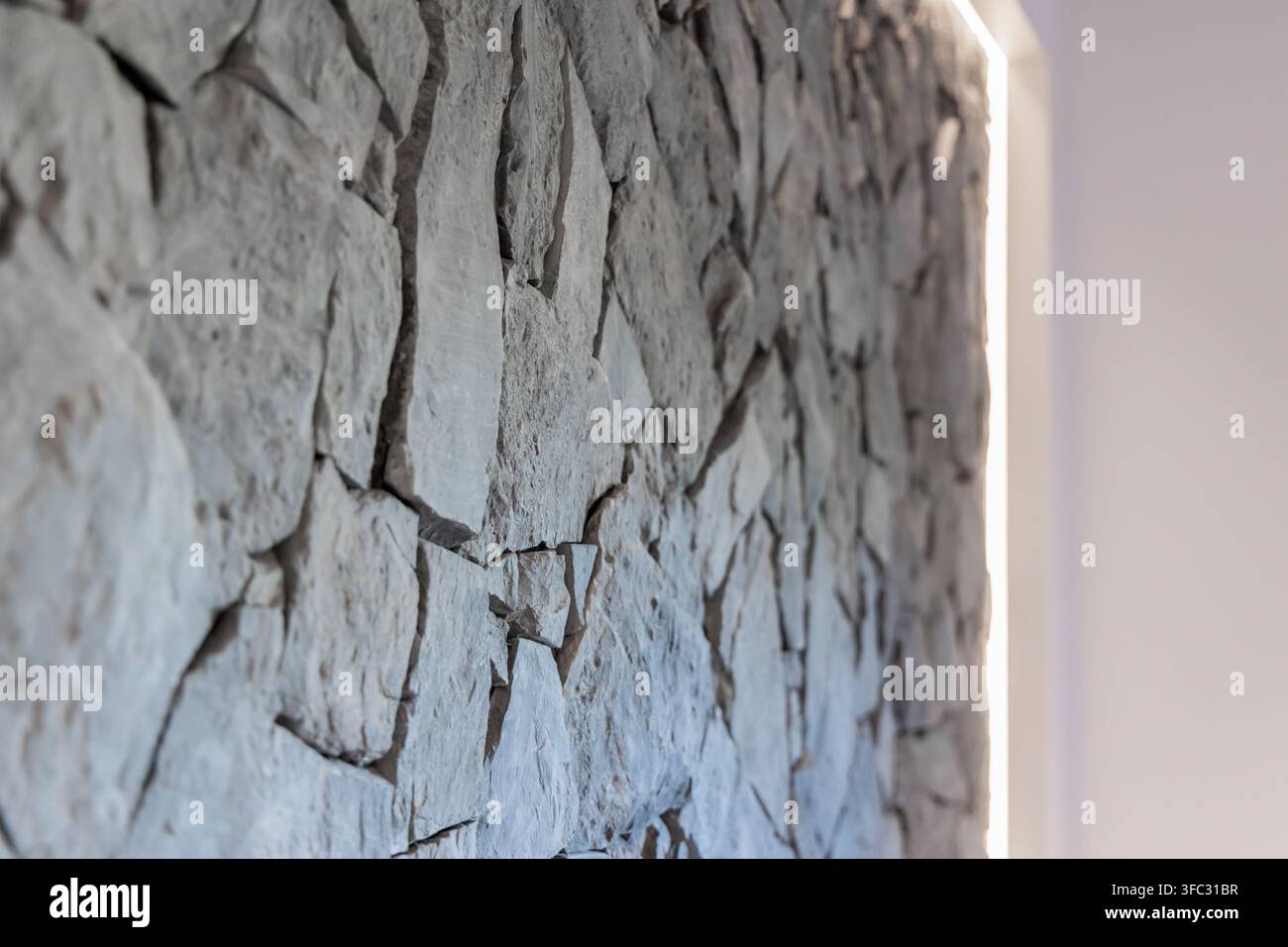 A close-up view of a rough-hewn stone wall surface, showcasing its natural texture and irregular shapes with a soft light illuminating the edge Stock Photo