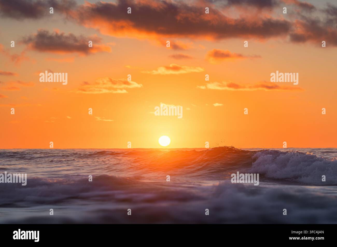 Bright setting sun over ocean waves during a fiery orange sunset Stock Photo