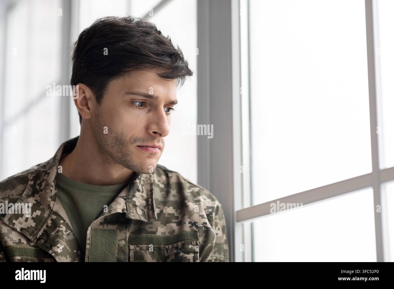 Thoughtful Young Man In Military Uniform Looking Out Of Window In Office Setting Stock Photo