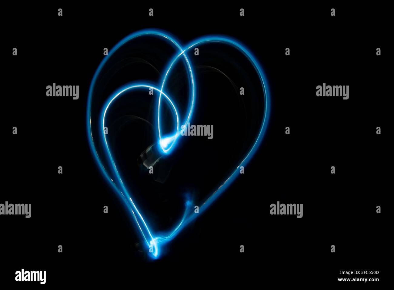 A romantic and modern long exposure photograph capturing a glowing neon blue light trail that forms the shape of a heart in darkness. Stock Photo