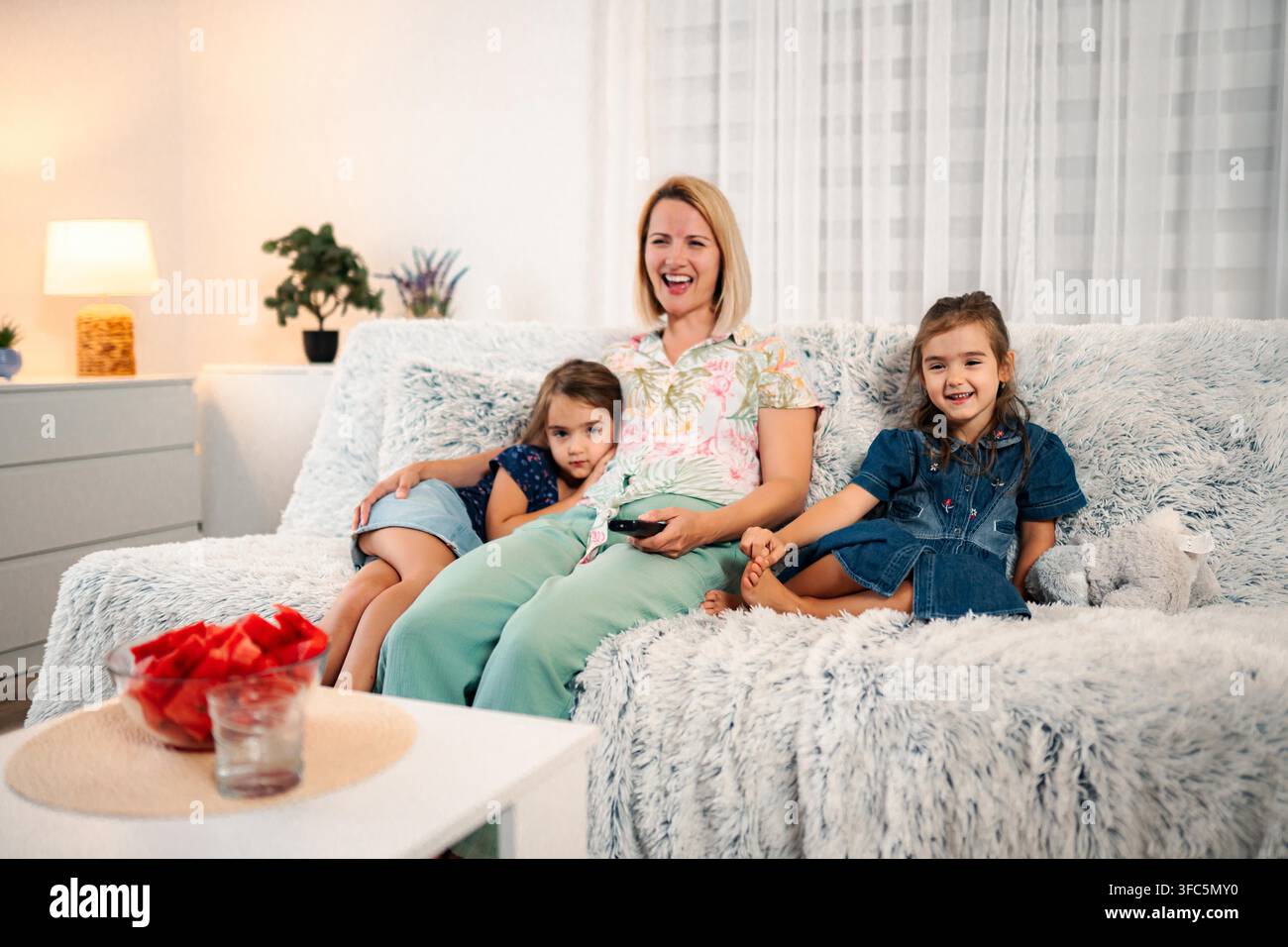 Mother and daughters relaxing on sofa watching tv together Stock Photo