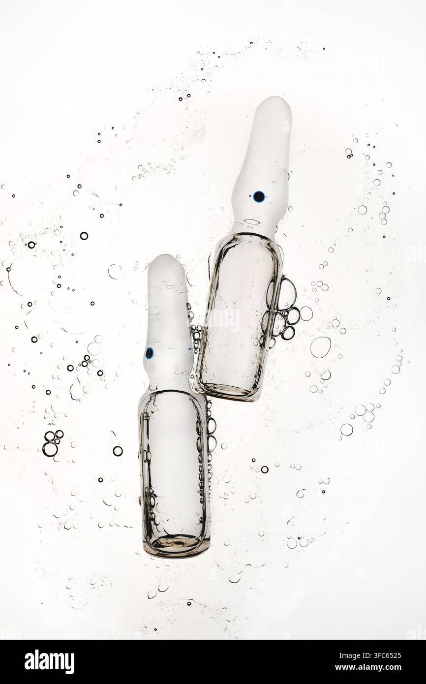 Two transparent glass ampoules floating in liquid with air bubbles Stock Photo