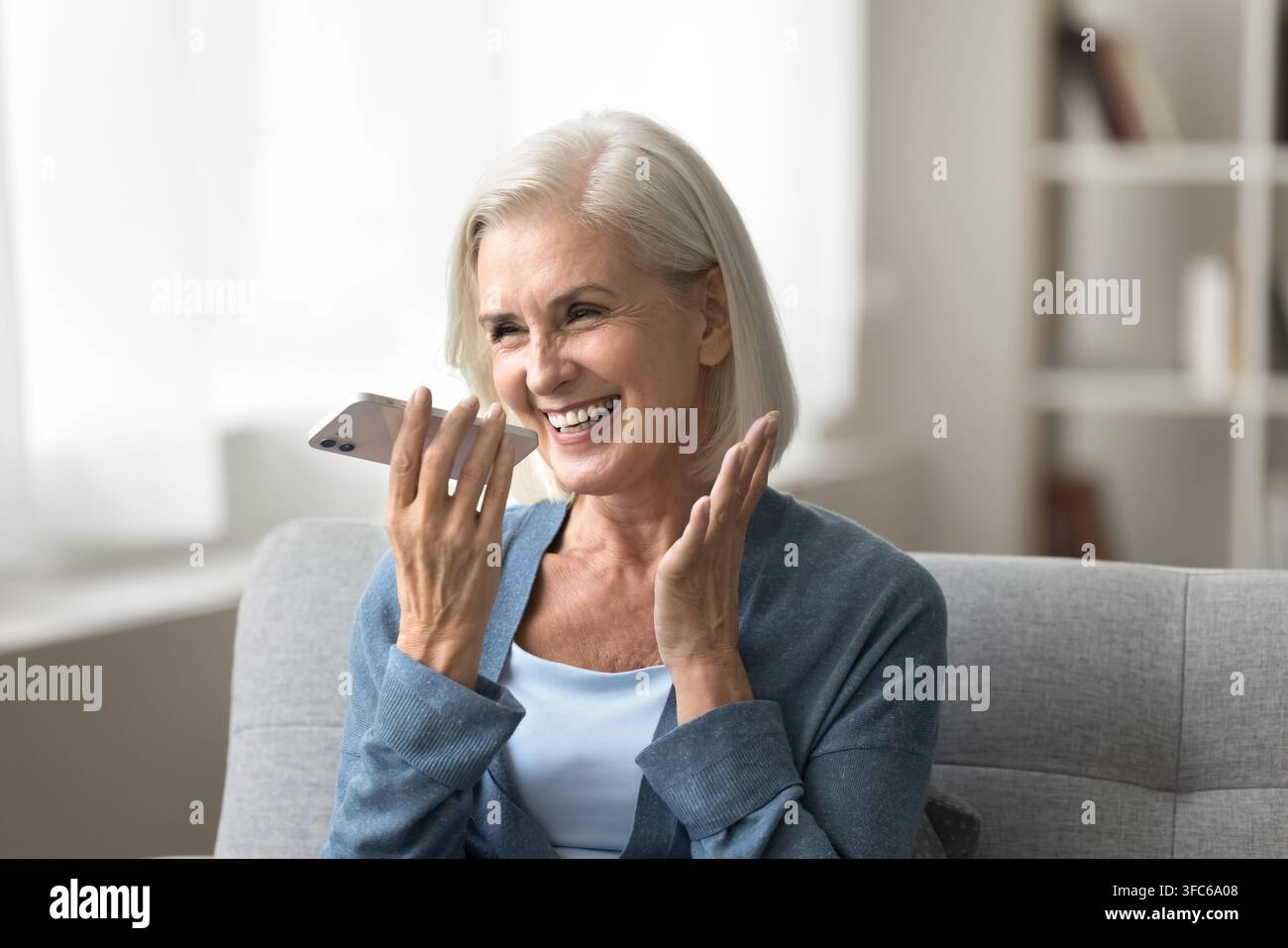 Cheerful elderly woman hold smartphone by mouth record vocal message Stock Photo