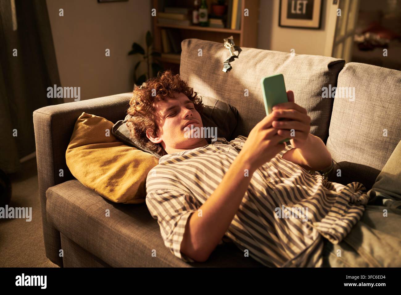 Man Lying on Sofa and Using Smartphone for Social Media Browsing Stock Photo