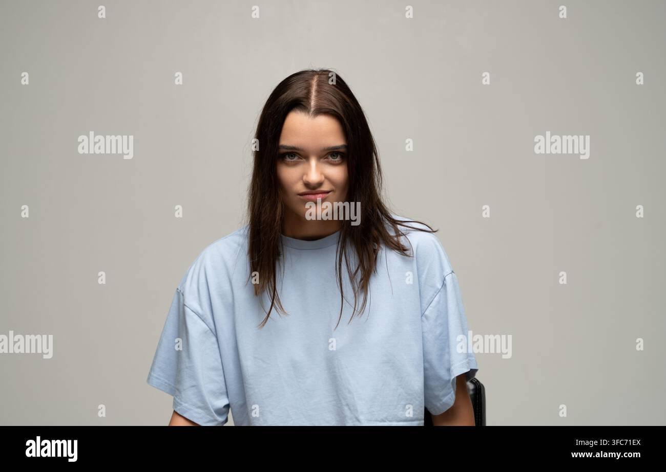 Confident brunette woman giving a subtle smirk, looking powerful and self-assured in studio portrait, expressing determination Stock Photo