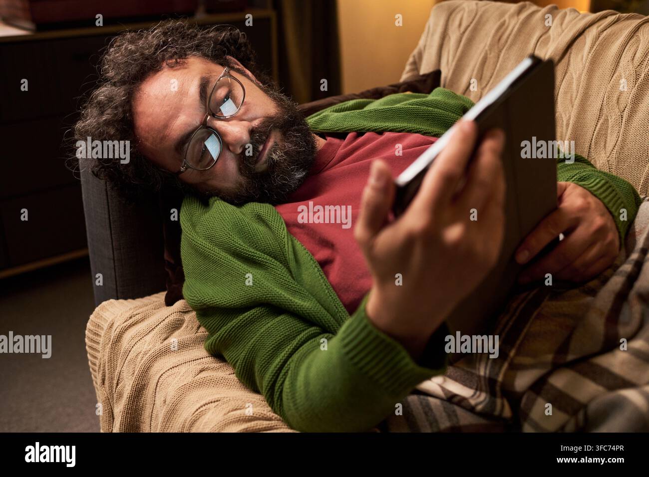 Middle Aged Man Lying on Sofa and Using Digital Tablet at Home Stock Photo