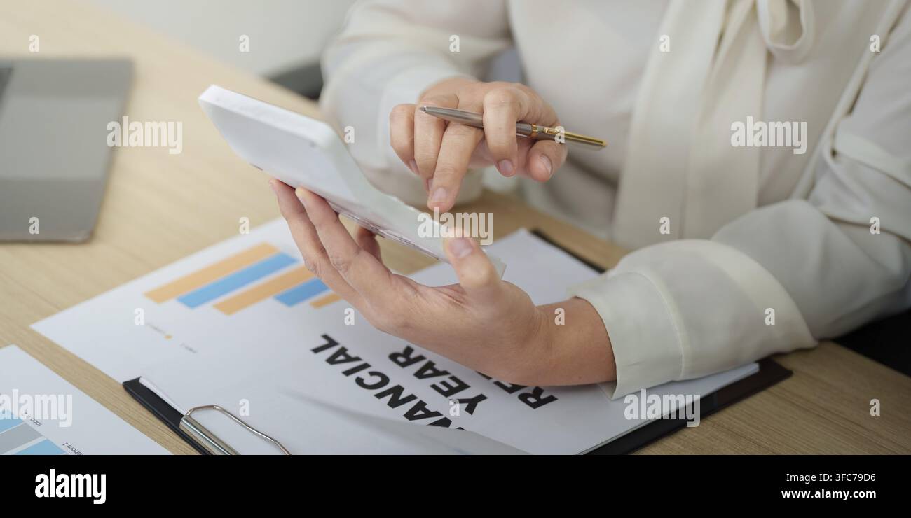 A businesswoman focuses on analyzing financial data using a tablet and is preparing for an annual financial report in a modern office Stock Photo