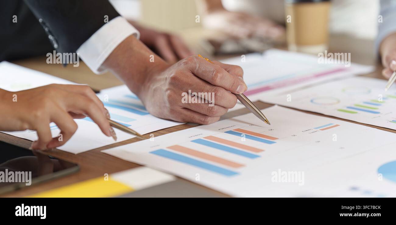 A diverse business team works together in a meeting and points to financial data and charts on paper. This image represents strategic planning and tea Stock Photo