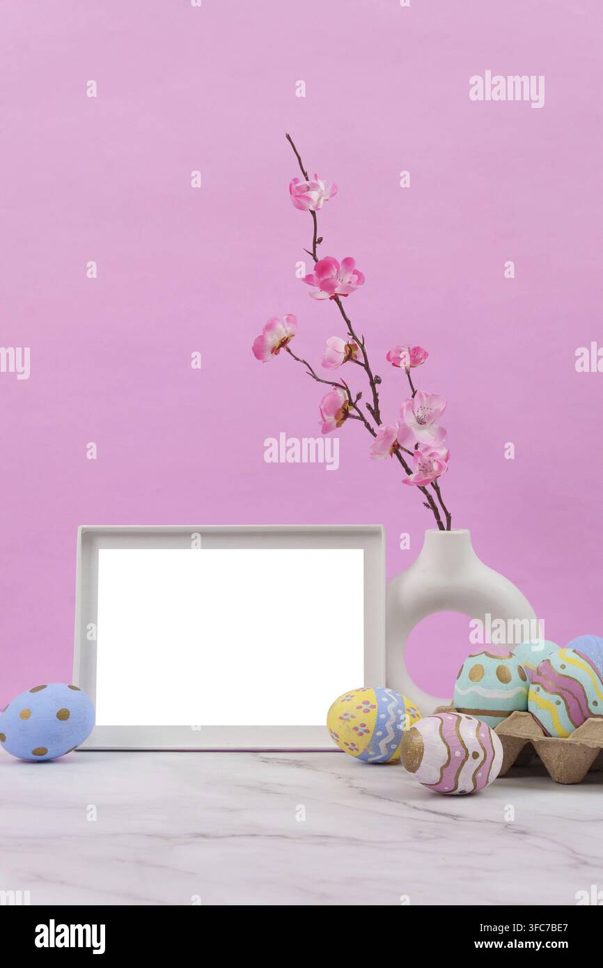 A delightful decor with an empty frame, cherry blossoms and colorful Easter eggs against a pink background Stock Photo
