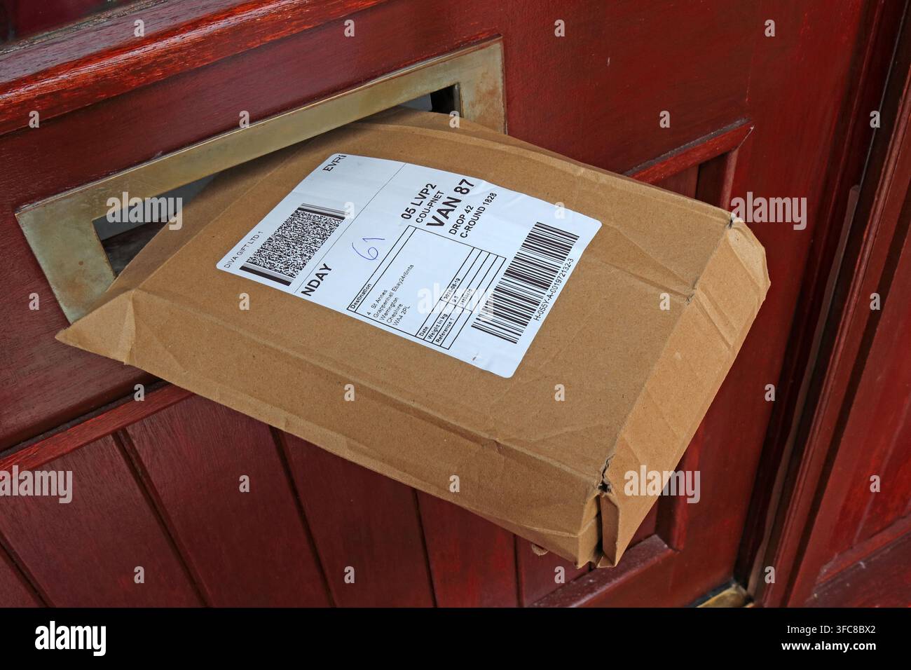 Evri parcel left partly protruding from a front-door letterbox, illustrating unattended home delivery and poor parcel security. Stock Photo