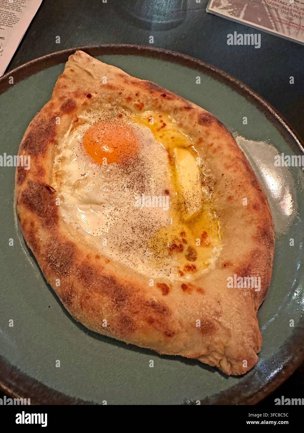 Georgian Ajaruli khachapuri Calzone-style folded pizza with a raw egg baked into the centre, served on a plate as a hot restaurant meal. Stock Photo