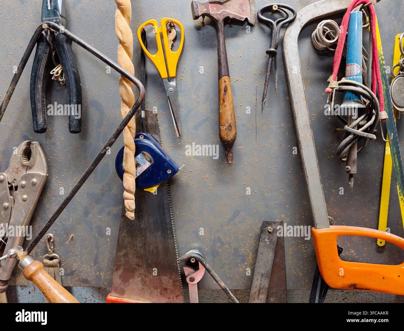 Various dirty and well used hand tools, including saws, pliers, hammers, and measuring tape, hanging neatly on a dusty workshop wall, representing cra Stock Photo