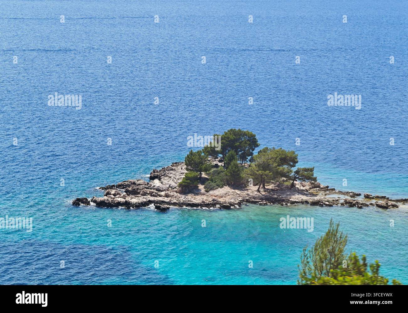 A small rocky islet crowned with pine trees rises from the crystal-clear turquoise waters, evoking a sense of peaceful isolation and natural beauty. - Smartphone Captured Stock Image